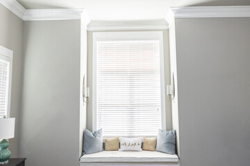 A light and bright gray master bedroom with a window seat for reading and relaxing - obrazy, fototapety, plakaty