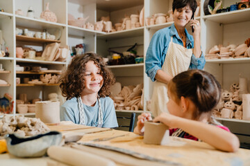 Female teacher talking on cellphone while working with kids in pottery class