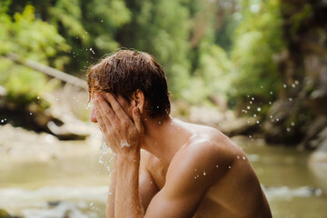 Young man splashing his face with water while resting by the mountain river