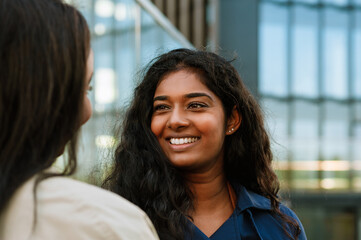 Two young multinational women smiling while standing at the city street