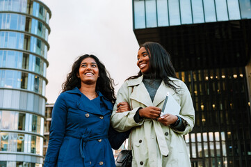 Two young joyful women walking outdoors at the city street