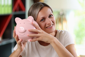 Happy woman holding big piggy bank in her hands and looking at camera close-up.