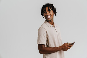 Young african man holding mobile phone and looking aside while standing isolated