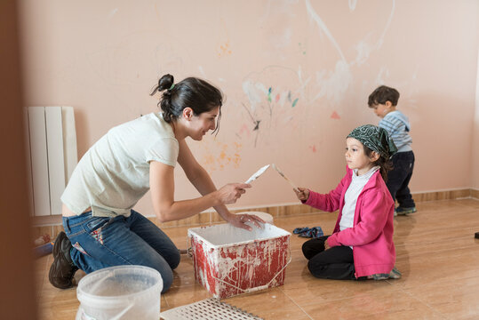 mother guides her children on how to paint the rooms of the house with a bucket full of white paint