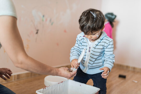 Dirty 2 years old boy helping painting at home