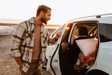 Happy young white man smiling while standing by car at seashore