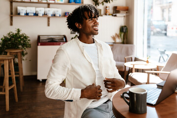 Excited young african man with laptop sitting in cafe indoors