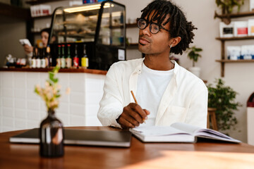 Young afro man taking notes while sitting at table in cafe