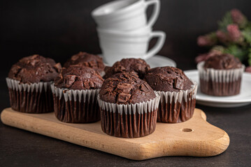 Blurred image of chocolate muffins on a wooden board in the foreground, in the background a cup of tea on a dark background.