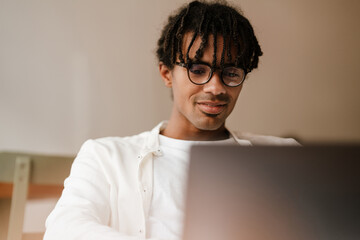 Young african american man smiling and using laptop in cafe indoors