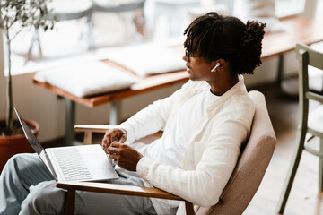 African man in eyeglasses using laptop computer while sitting in cafe