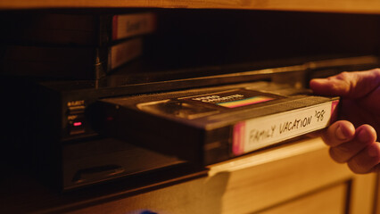 Close Up of a Person Inserting a VHS Cassette in a Player with Nostalgic Vacation Footage from Home Video Camera. Retro Nineties Technology Concept. Old VCR with Shallow Depth of Field and Bokeh.