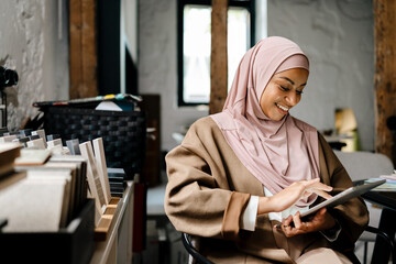 Cheerful arabian woman working on tablet computer at workshop