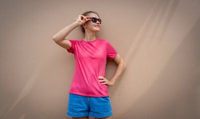 Female model wearing pink blank t-shirt on the background of an sandy wall.