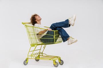 Cheerful middle-aged woman sitting in shopping cart isolated