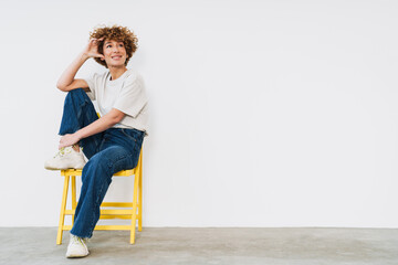 Middle-aged woman sitting on yellow chair and looking away at copy space isolated