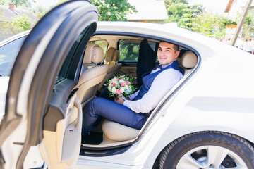 stylish groom sits in the car and waits for the bride with a bouquet of flowers. Preparing for the wedding ceremony.