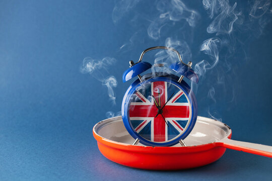 Alarm clock with the UK flag in a pan with smoke on a blue background. Concept time for change. Copy space.