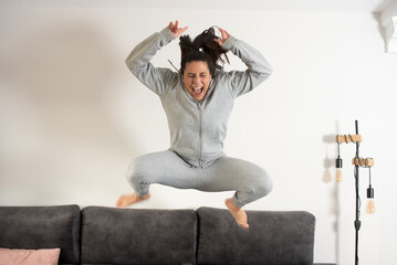 girl jumping on the sofa dressed in a grey tracksuit and dancing with mobile phone headphones