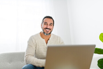 man with black hair using laptop at home sofa