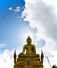 Golden Buddha with his head hidden the sun in a halo in from of a blue sky with some clouds