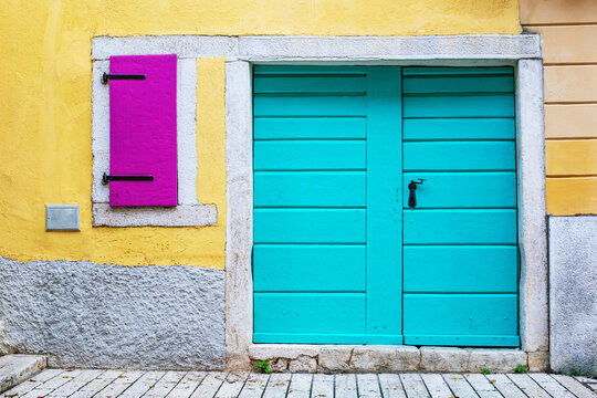 Blue door and window with purple shutters against a yellow wall in old house