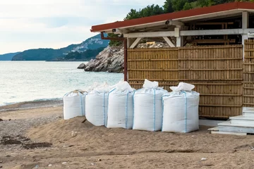 Foto op Canvas There are many large white sandbags on the beach for flood protection. Sandbags to protect buildings and coastal structures to protect against tsunamis and floods. water protection structures. © Григорий Галасюк