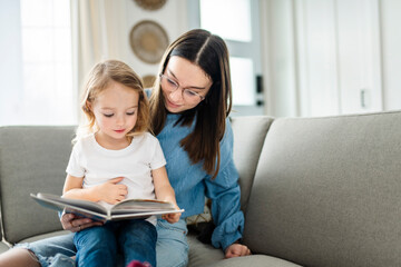 happy kid sitting on sofa with babysitter teen holding book