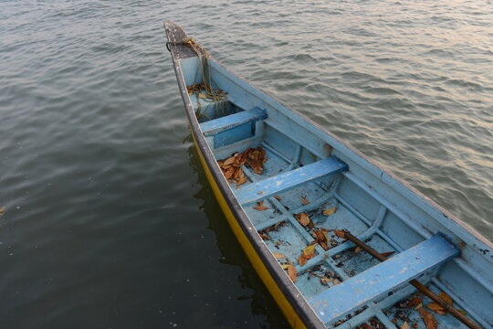 A small empty blue and yellow wooden row boat with leaves inside on a calm sea 