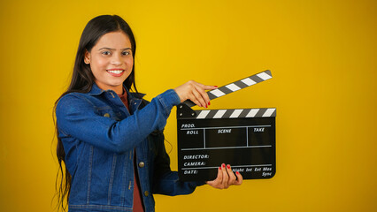 Beautiful young Asian Indian woman standing holding clapperboard, clapper board used in film making, isolated on color background studio portrait - obrazy, fototapety, plakaty