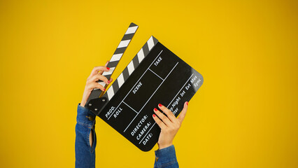 Hand is holding clapper board or clapperboard or movie slate, used in film production and cinema ,movies industry isolated over yellow background. - obrazy, fototapety, plakaty