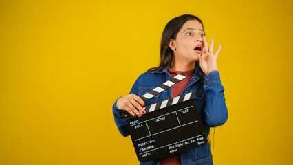 Beautiful young Asian Indian woman standing holding clapperboard saying something, clapper board...