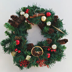 Christmas wreath handmade from artificial spruce branches, Christmas decorations, pine cones and dried fruits on white