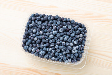 A lot of big ripe blueberries in plastic bowl on a white wooden table. Healthy nutrition, vitamins, natural food, tasty snack from wild forest