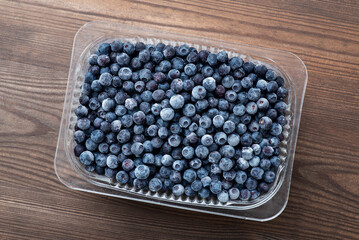 Transparent plastic bowl full of big ripe blueberries on dark wooden background. Healthy food for winter, vitamins and juicy sweet snack concept