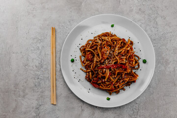 Spicy udon with chicken on a white plate on a gray background.Top view
