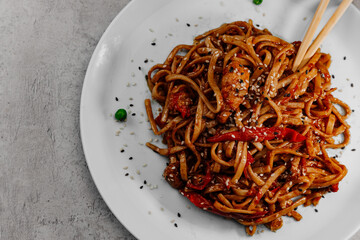 Spicy udon with chicken on a white plate on a gray background.Top view