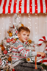 Young cheerful boy in winter sweater is posing on Christmas toy bicycle in decorated room with tree. Holiday concept.
