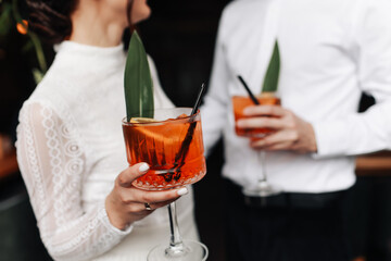 hands of woman and man are clinking, cheers with glasses of Spritz cocktail. Couple celebrating wedding, anniversary with Aperol spritz cocktails, with orange and greens Refreshing alcoholic drink