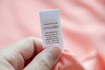 Hand hold and reading at white laundry care washing instructions clothes label on pink shirt