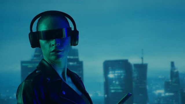 Portrait of cyberpunk girl with a smartphone in a glasses and headphones. Beautiful futuristic young woman on the background of city scyscrapers.
