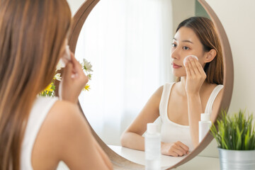 Obraz na płótnie Canvas Happy beauty, attractive asian young woman, girl looking reflect in mirror, hand holding cotton pad, applying facial wipe on her face remover makeup, essence or lotion for treatment, skin care routine