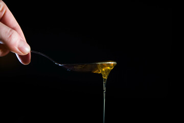 Close-up of honey dripping  from spoon on a black background. Copy space.