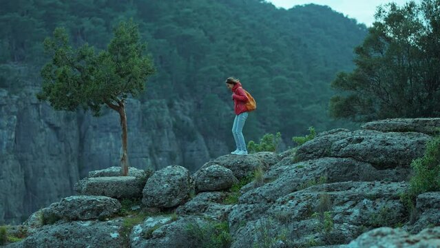 side view of tourist hiker girl in red jacket with backpack walks on edge cliff and overlooking big canyon, panoramic view. Tazi Canyon is common tourist destination in Turkey