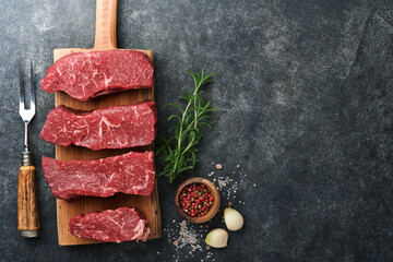 Raw steaks. Top blade steaks on wood burning board with spices, rosemary, vegetables and...