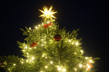 Weihnachtsbaumspitze mit goldenem leuchtendem Stern, brennender Lichterkette und roten...