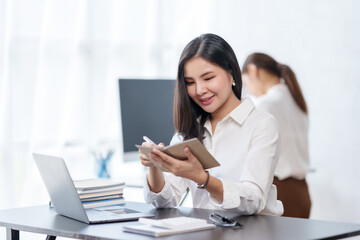 Beautiful Asian businesswoman working on paperwork at her desk in the office review work from different department, take minute of meetings report other document.