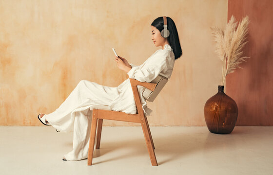 Side view of asian woman chatting with friends on phone, listening to music in headphones