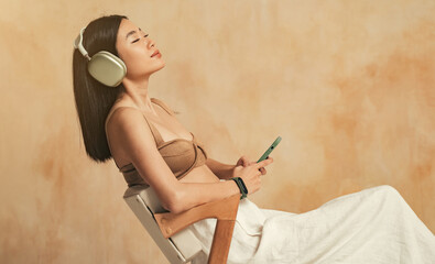 Side view of young asian female in headphones enjoying favorite songs using phone music app