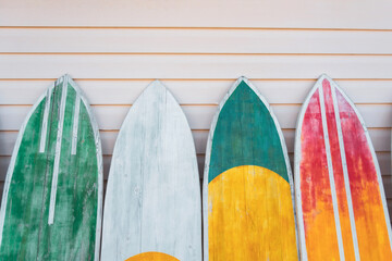 Several surfboards of different colorful saturated yellow, green, red colors lined up against the wall.